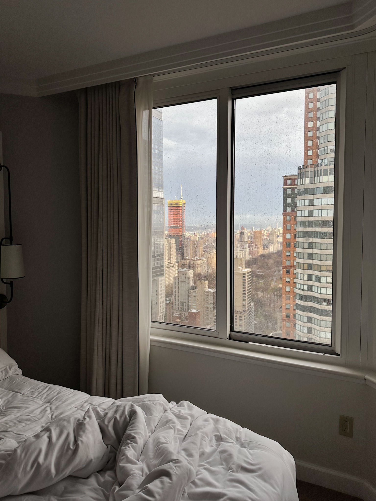 Bed in front of a window where you can see New York City's skyline